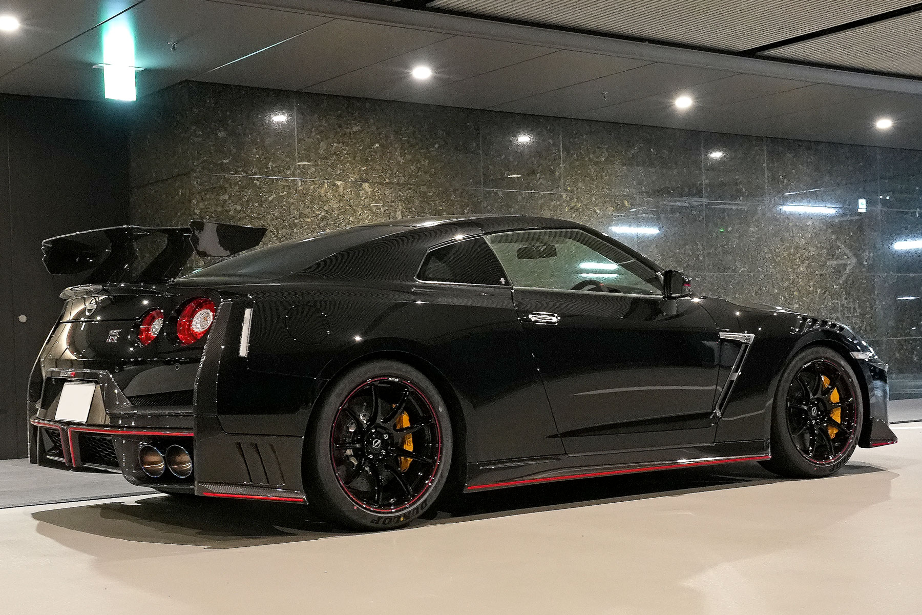 2025年モデル GT-R NISMOスペシャルエディション。メテオフレークバラックパールのボディに、NISMO専用カーボンエアロと赤いアクセントを特徴とするハイパフォーマンスモデルのリヤビュー画像